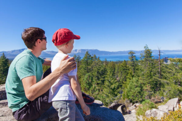 family of father and his son resting after hike and enjoying gorgeous view at lake tahoe at summer